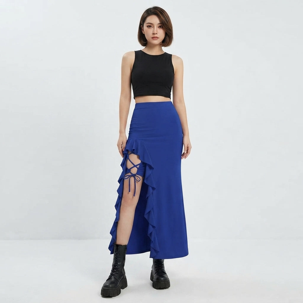 A woman modeling a two-piece outfit consisting of a black sleeveless crop top and a high-waisted royal blue wrap skirt with a ruffled hem and side cutout tied with blue straps, paired with black ankle boots, against a plain white studio background.