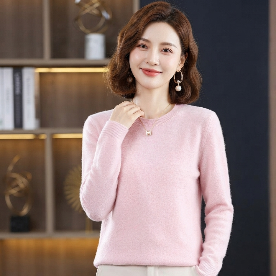 A woman wearing a light pink long-sleeve knit sweater and white pants, standing in front of a dark wood and black paneled background.