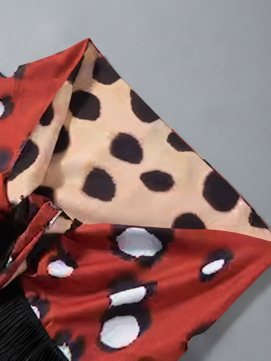 A close-up of a patterned fabric accessory, likely a scarf or sash, featuring a split design with a beige and black leopard print on one side and a red and black spotted print on the other, with a black pleated fabric visible at the bottom.