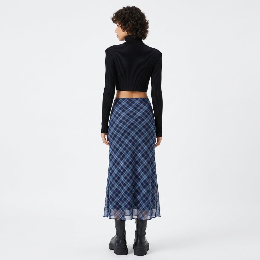 A model is shown from the back wearing a black ribbed long-sleeve crop top and a blue plaid midi skirt with black boots, set against a plain white studio background.