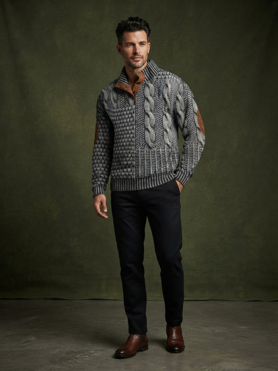 A man modeling a gray and black cable-knit quarter-zip sweater with brown leather patchwork details on the sleeves, paired with dark trousers and brown leather shoes, against a dark olive green studio backdrop.