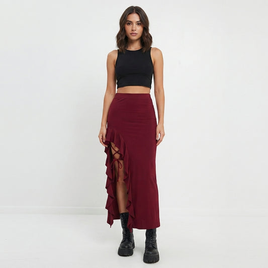 A woman modeling a high-waisted, dark red ruffled asymmetrical midi skirt paired with a black crop top and black lace-up ankle boots, set against a plain white studio background.