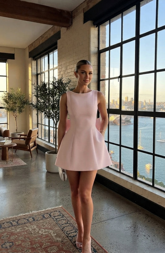 a woman wearing a pink dress stands in front of a large window overlooking a city