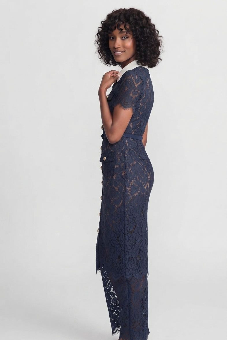 A woman modeling a navy blue lace midi dress with short sleeves, a white collar, and a backless design, photographed against a light gray studio background.
