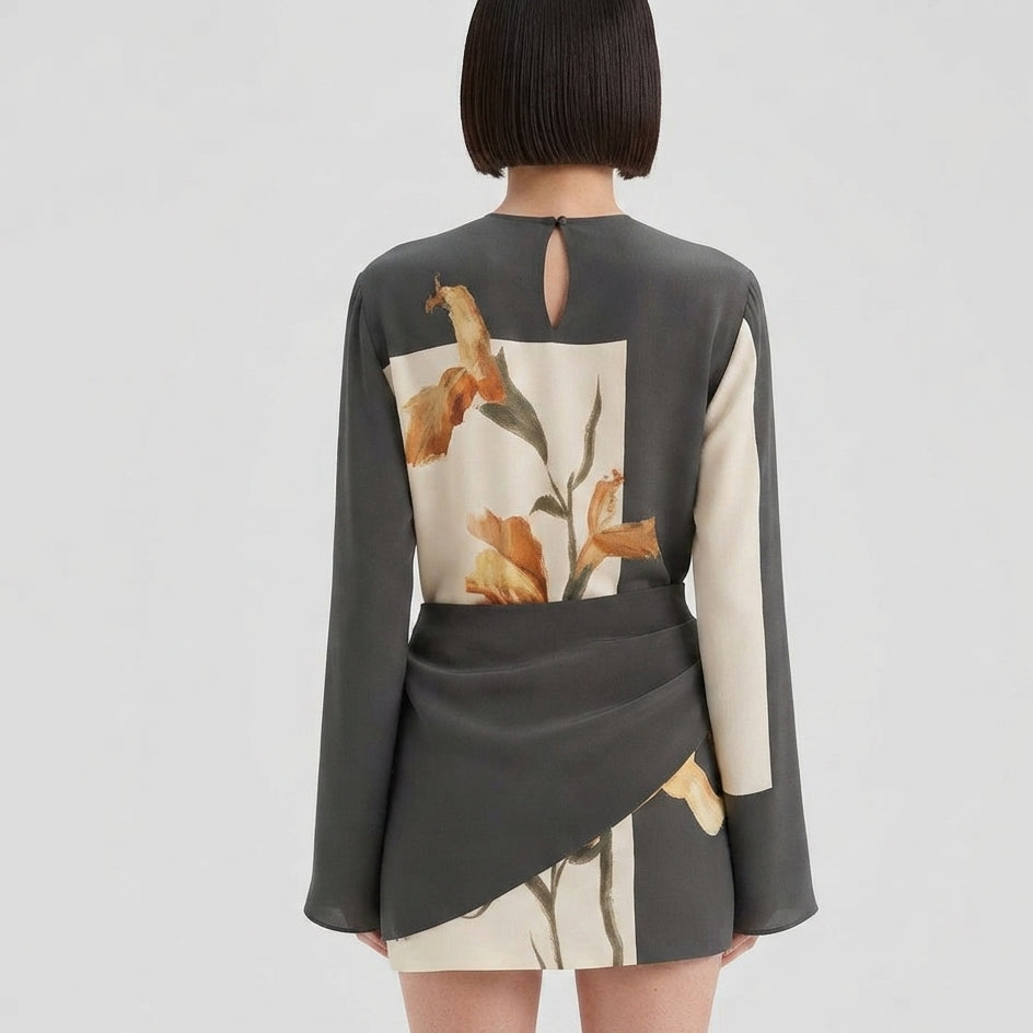 A model shown from the back wearing a dark gray long-sleeve mini dress with a large cream panel featuring a floral print on the back.