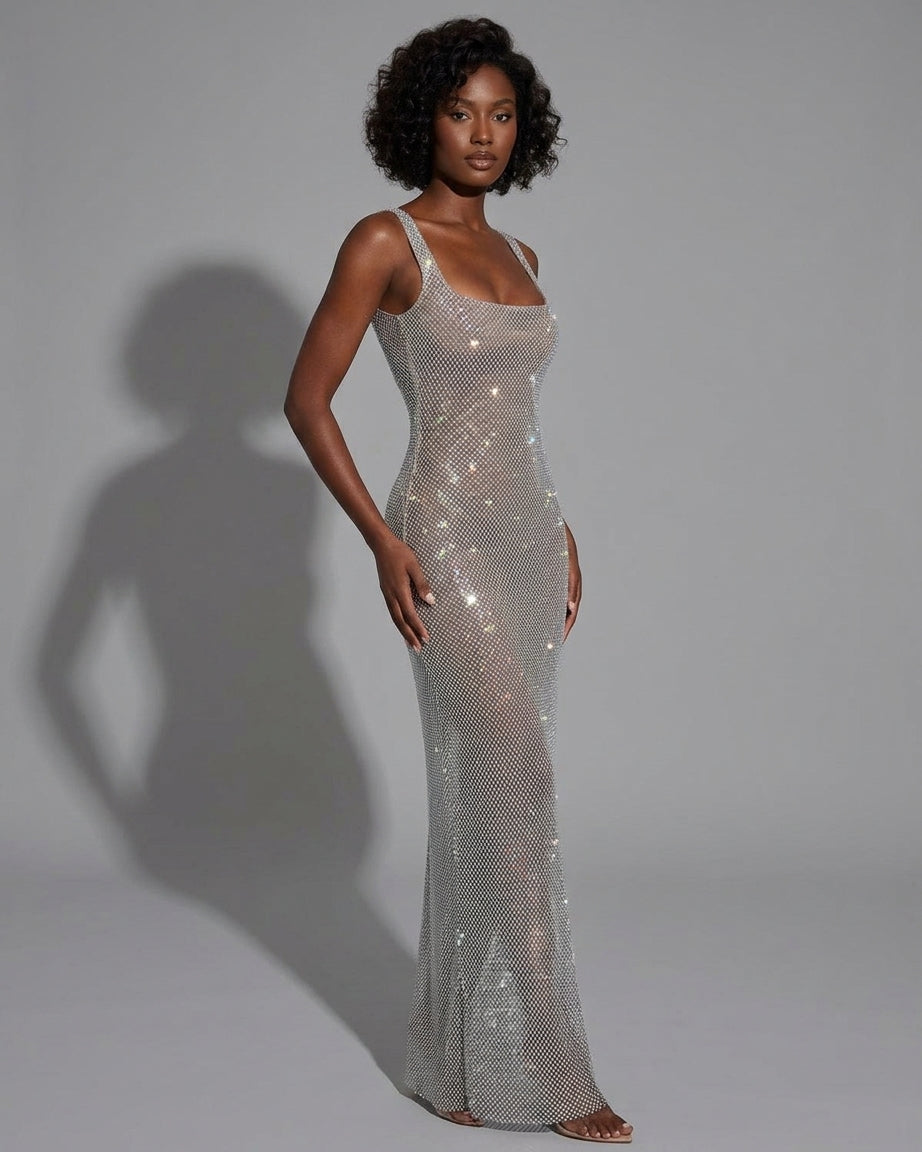 A woman modeling a floor-length, sleeveless silver sequin gown against a light gray studio background with a soft shadow cast to the left.