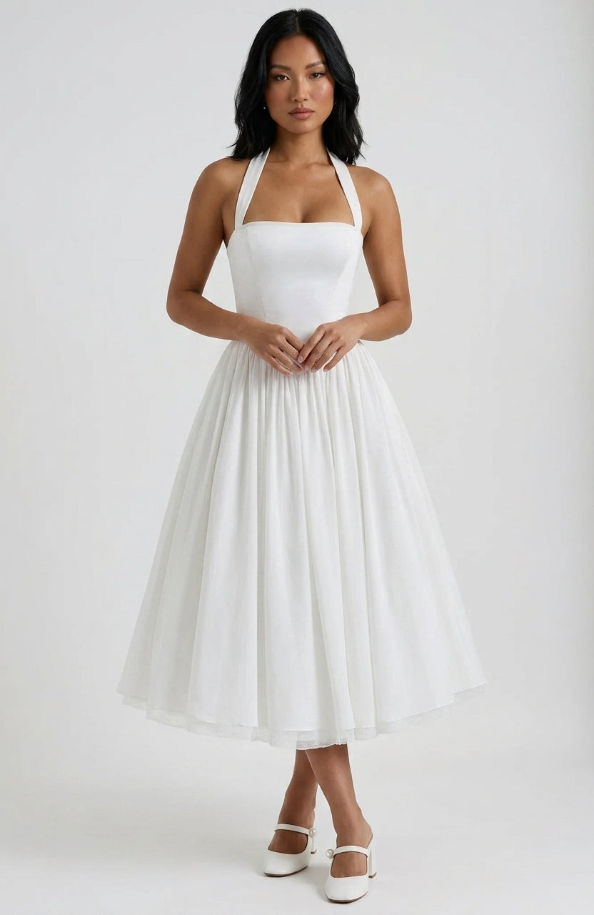 A woman modeling a white halter-neck midi dress with a structured bodice and a full, flowing skirt, paired with white Mary Jane shoes, against a light gray studio background.