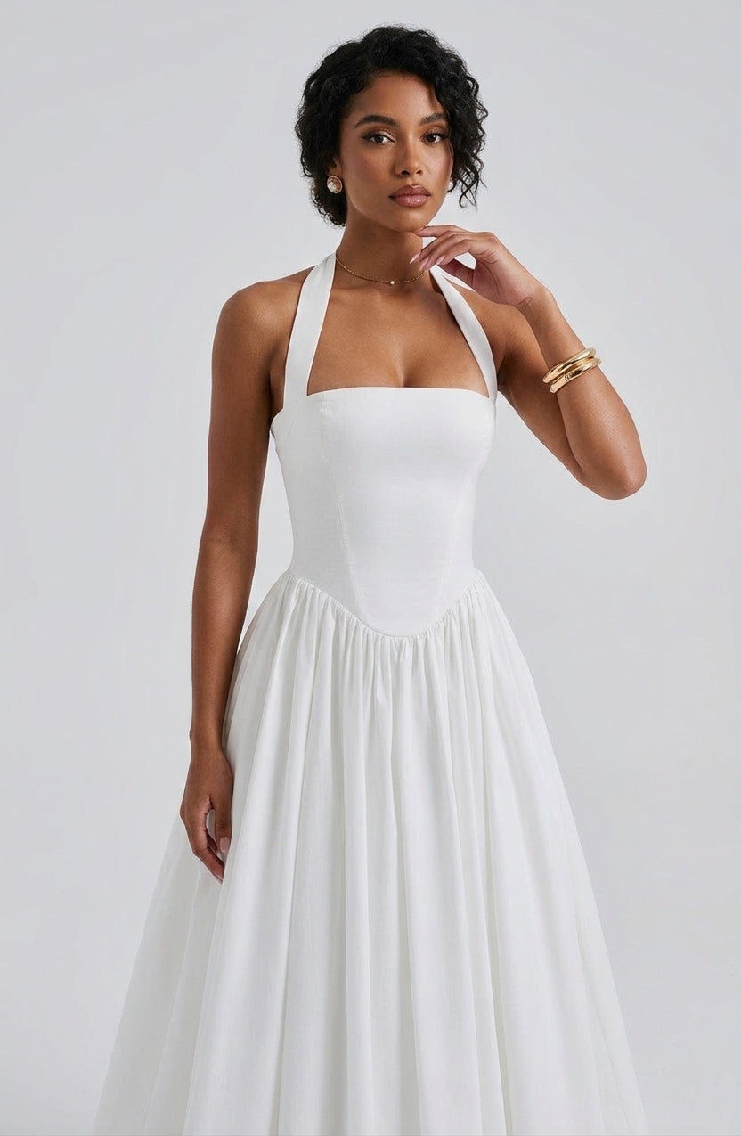 A woman modeling a white halter-neck A-line dress with a structured bodice and flowing skirt, photographed against a light gray studio background.