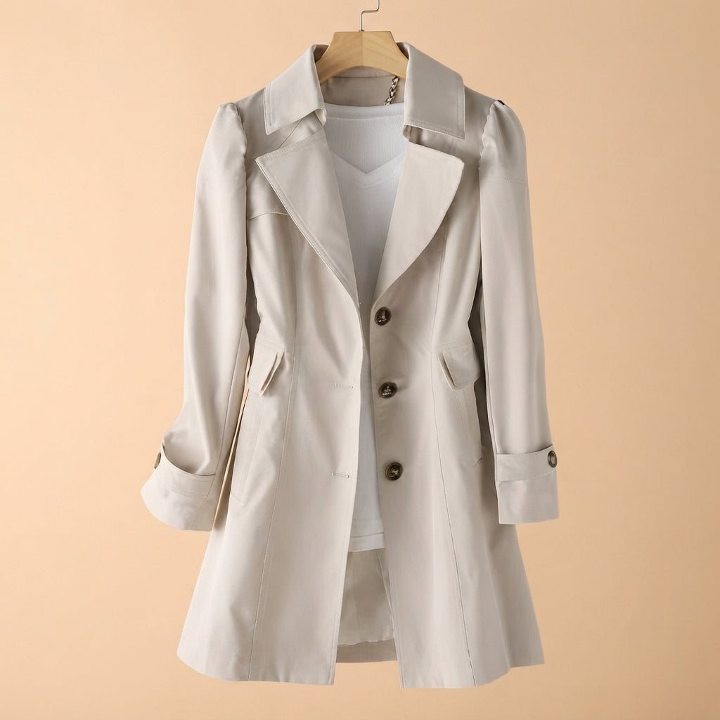 A light beige trench coat with a double-breasted button closure, displayed on a wooden hanger over a white top against a solid beige background.