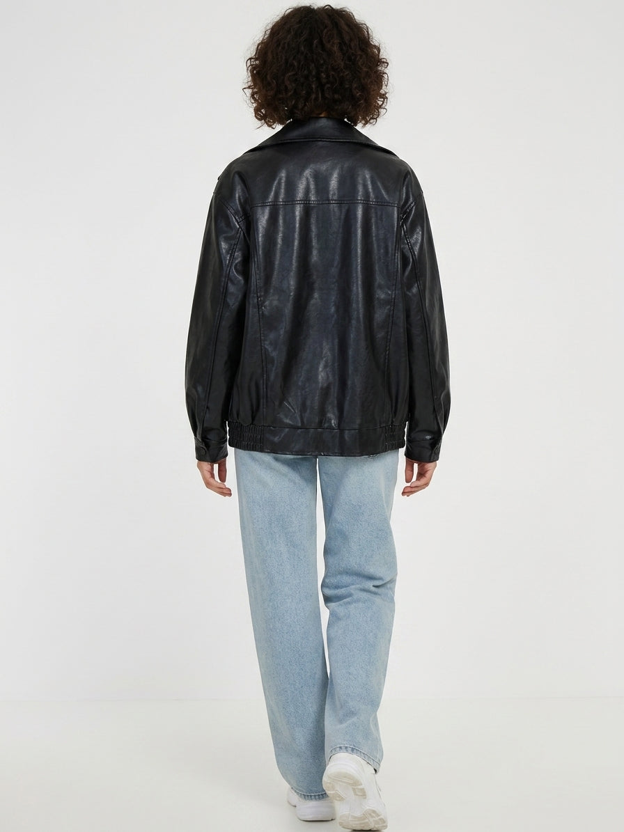 A person shown from the back wearing a black faux-leather jacket, light-wash blue jeans, and white sneakers against a plain white studio background.