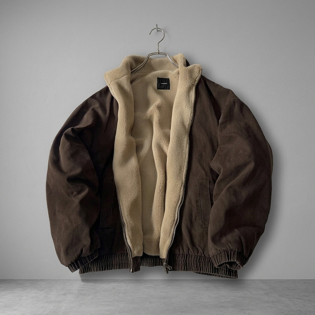 A brown suede jacket with a beige sherpa lining, hanging on a metal hanger against a neutral gray background.