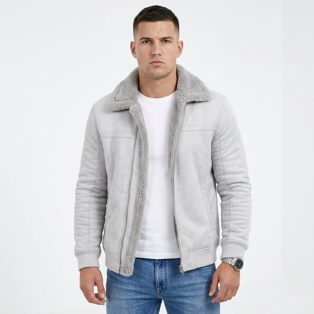 A man wearing a light gray suede jacket with a plush gray sherpa collar, layered over a white t-shirt and blue jeans, photographed against a plain white studio background.