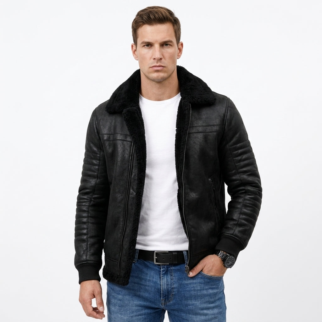 A man wearing a black leather aviator-style jacket with a black shearling collar, layered over a white t-shirt and blue jeans, photographed against a solid white background.