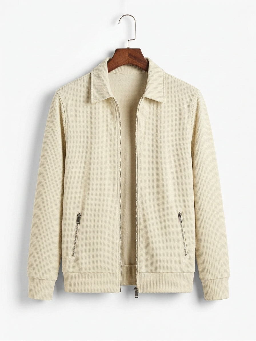 A cream-colored waffle-knit zip-up jacket with a collar and two zippered hand pockets, hanging on a wooden hanger against a plain white background.