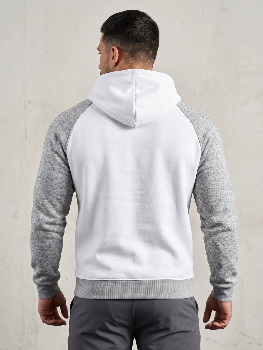 A man viewed from the back wearing a raglan hoodie with a white body and heather gray sleeves, paired with gray pants, against a light textured wall.