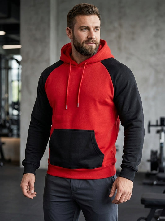A man wearing a red and black colorblock pullover hoodie with a kangaroo pocket, standing in a gym environment.