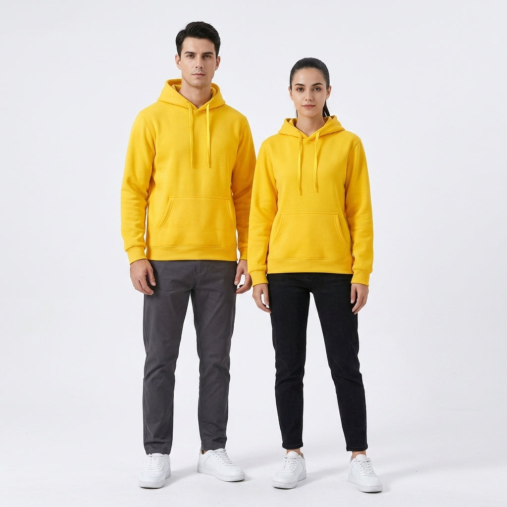 A man and a woman modeling matching bright yellow pullover hoodies with drawstrings and kangaroo pockets, paired with dark gray and black pants respectively, against a plain light gray studio background.