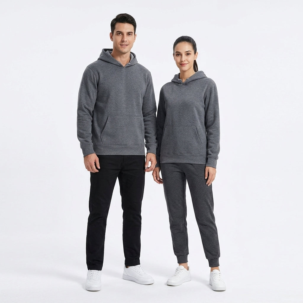 A man and a woman modeling matching dark gray hoodies and jogger sweatpants sets against a plain white studio background.