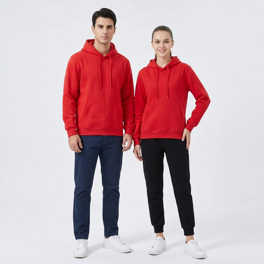 A man and a woman modeling matching bright red pullover hoodies with drawstrings and kangaroo pockets, paired with navy pants, black joggers, and white sneakers on a light gray studio background.