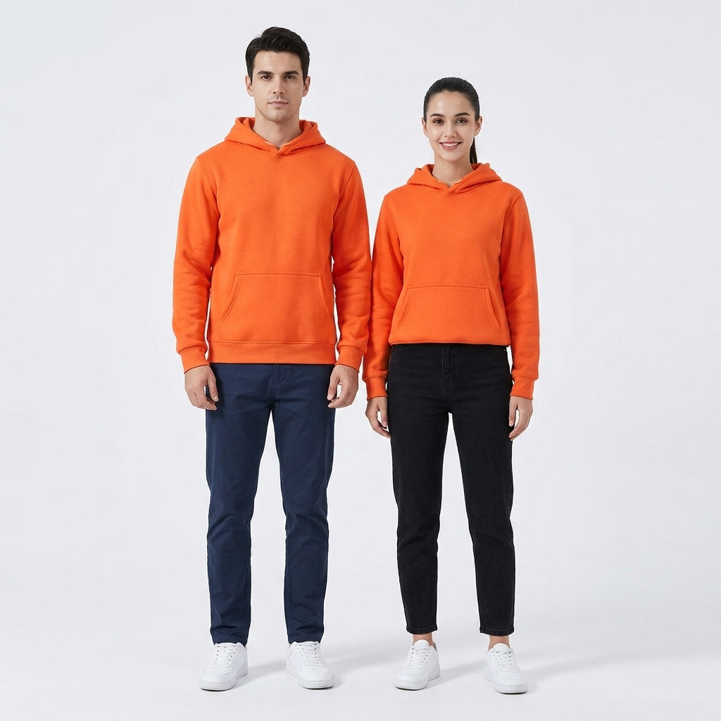 A man and a woman modeling matching bright orange hooded sweatshirts, standing against a clean white studio background. The man wears navy pants and white sneakers, while the woman wears black pants and white sneakers.