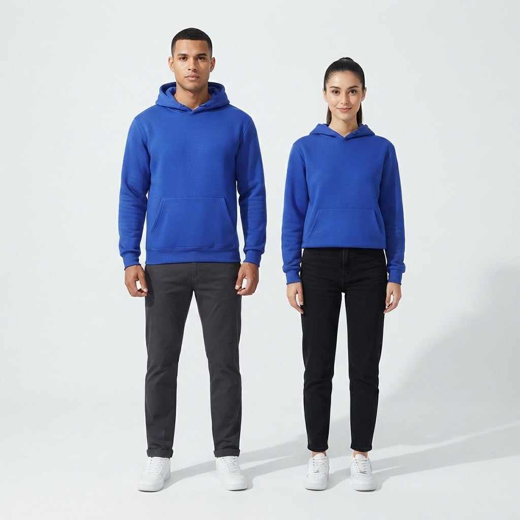 A man and a woman modeling matching royal blue pullover hoodies, standing against a clean light gray studio background. The man wears dark gray pants and white sneakers, while the woman wears black pants and white sneakers.
