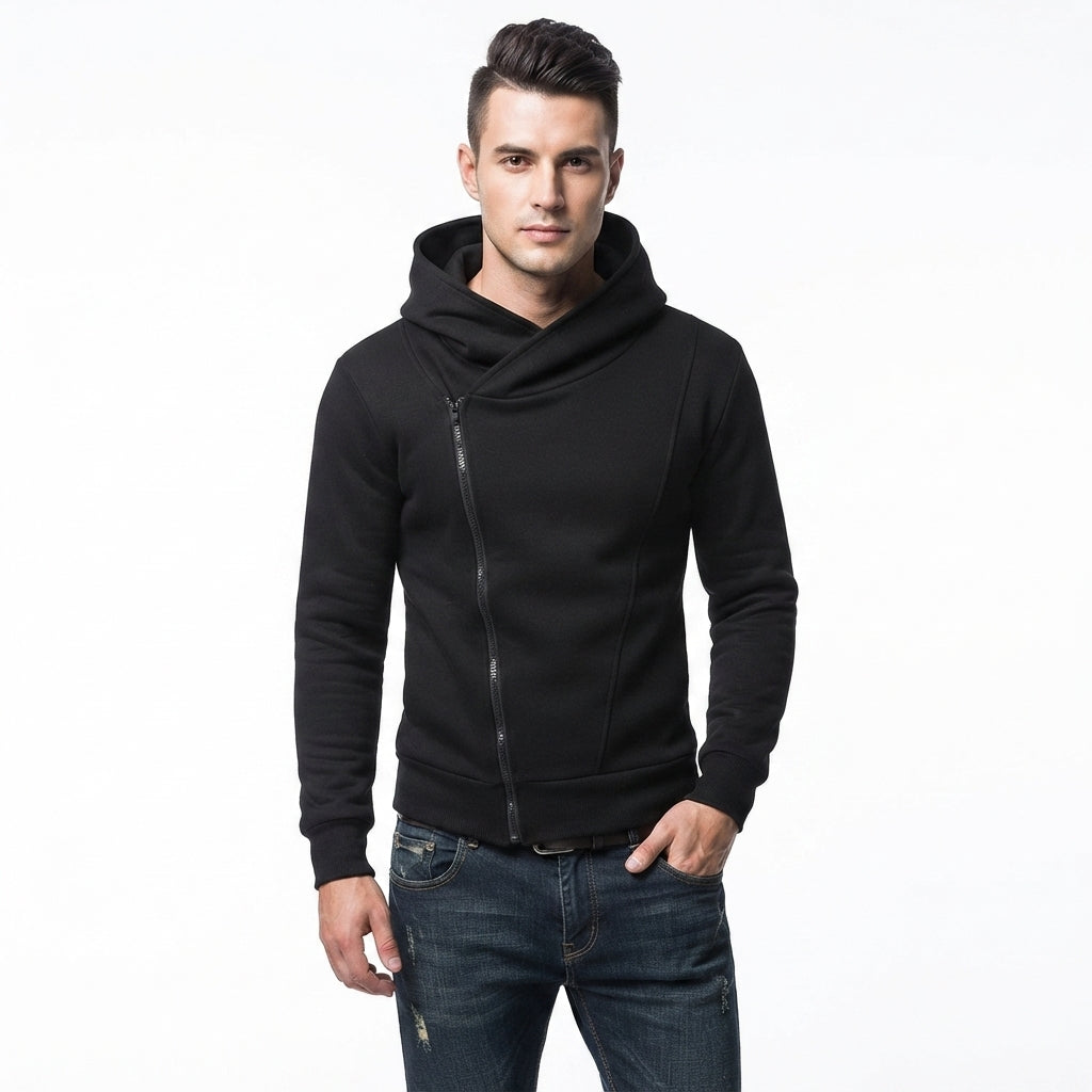A man wearing a black asymmetrical zip-up hoodie with a cowl neck and dark blue jeans, standing against a plain white background.
