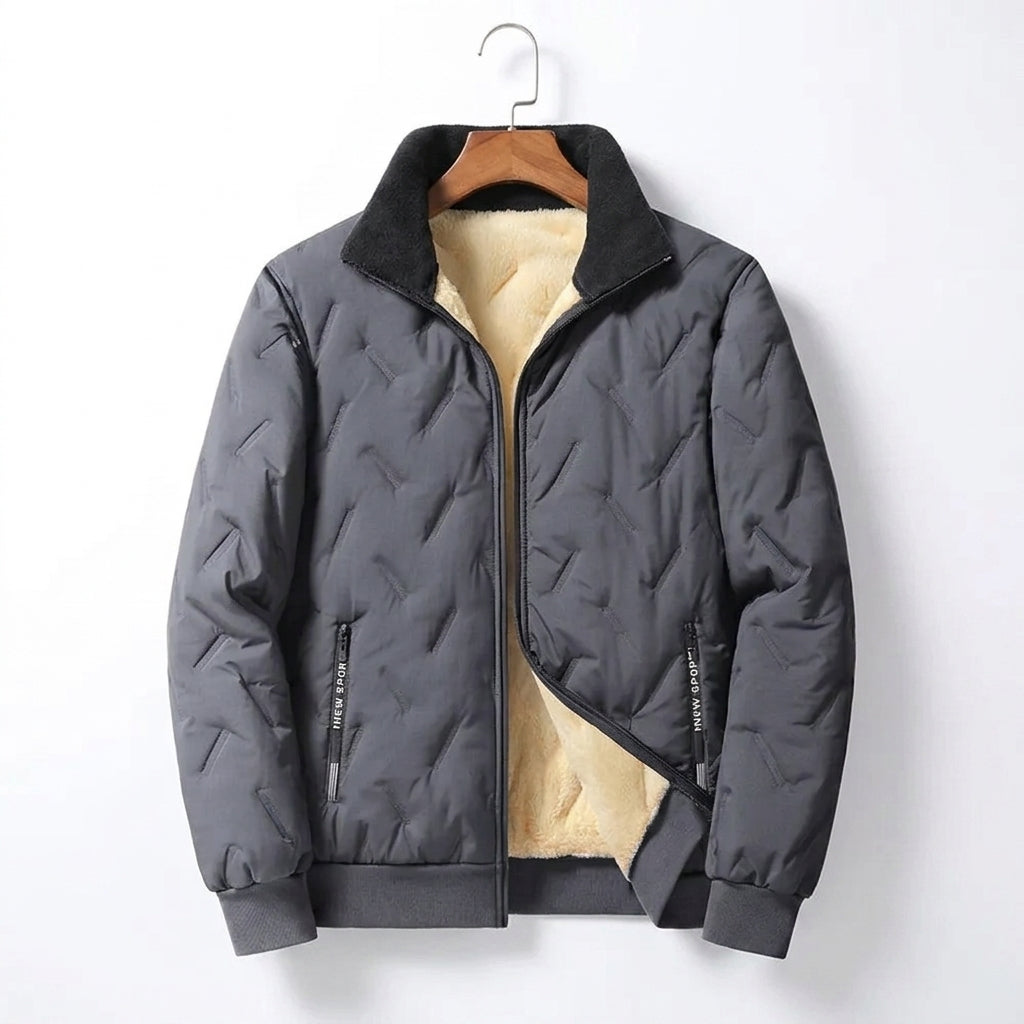 A dark gray quilted men's jacket with a black collar and a beige sherpa lining, hanging on a wooden hanger against a white background.