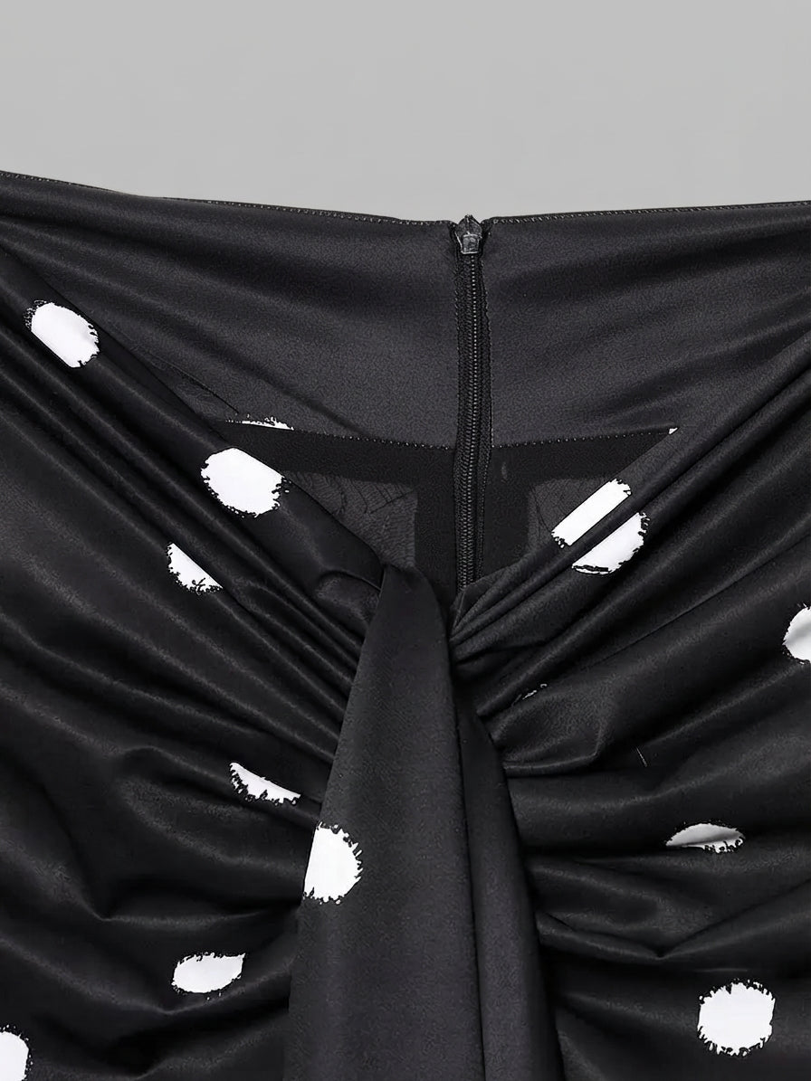Close-up of a black ruched garment with white polka dots and a central zipper, shown against a plain gray background.