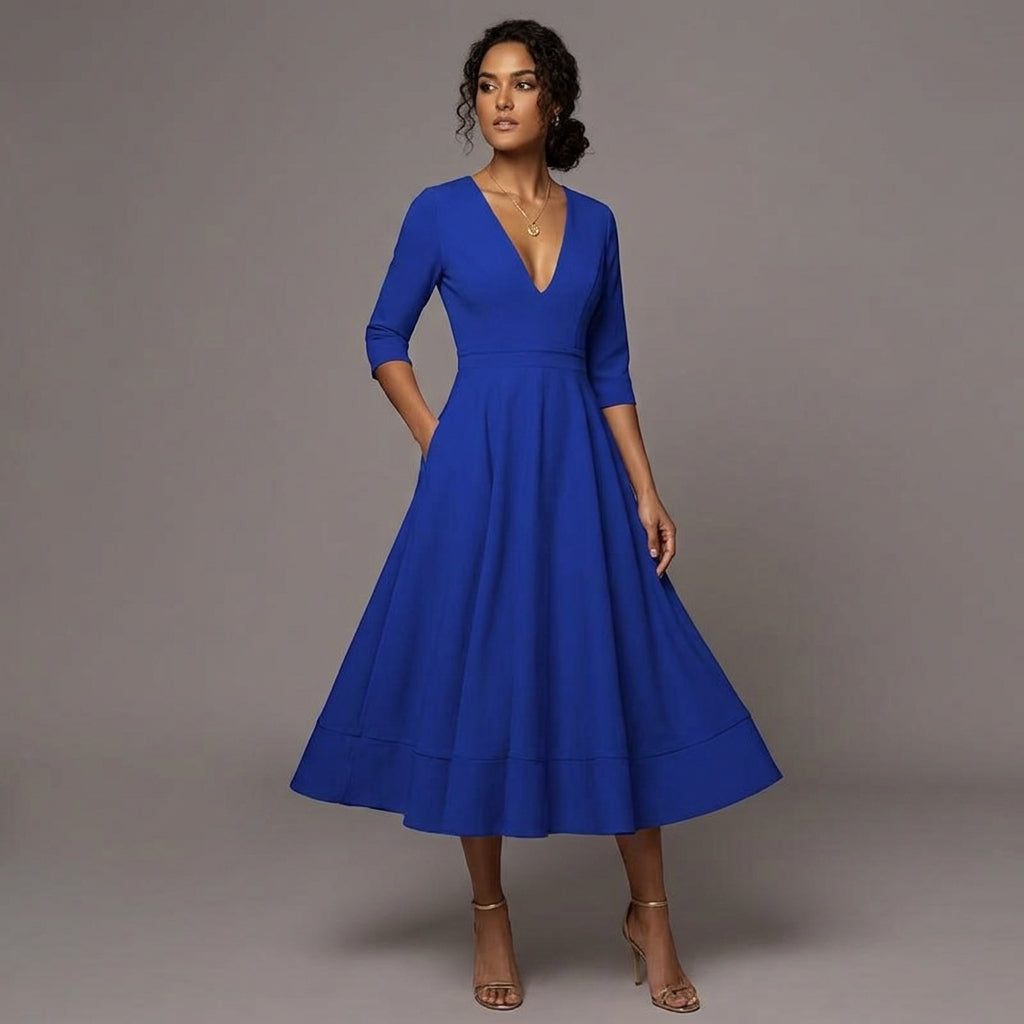 A woman modeling a royal blue midi dress with three-quarter sleeves, a deep V-neckline, and a flared skirt, posed against a solid gray studio background.