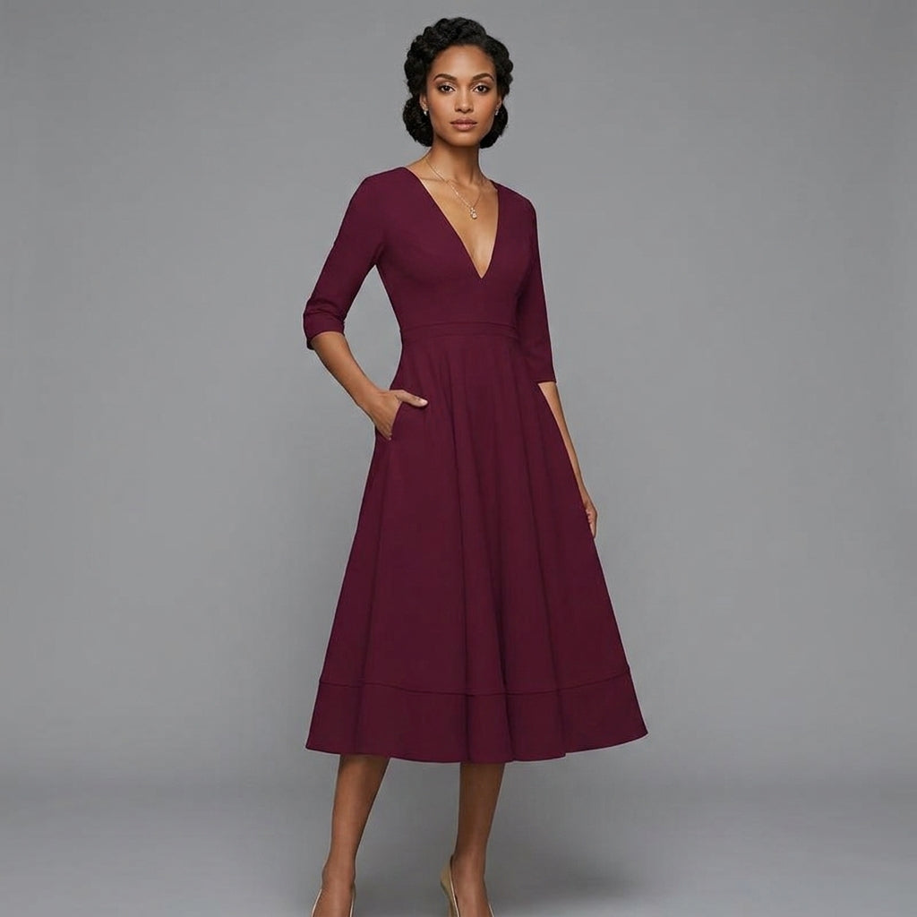 A woman modeling a knee-length, three-quarter sleeve V-neck dress in deep burgundy with side pockets, set against a solid gray studio background.