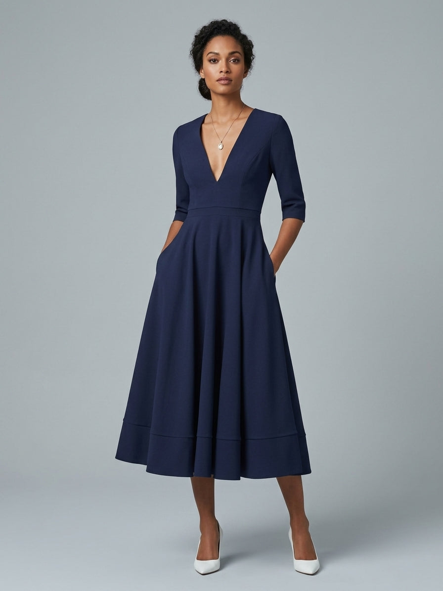 A woman modeling a navy blue midi dress with a deep V-neck, elbow-length sleeves, side pockets, and a flared skirt, paired with white heels against a light gray studio background.