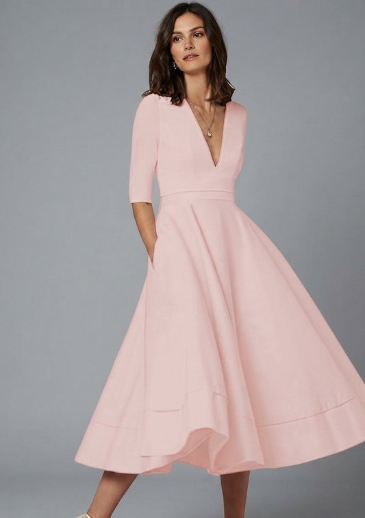A woman modeling a light pink midi dress with a deep V-neckline, elbow-length sleeves, a defined waist, and a flared skirt, set against a solid gray studio background.
