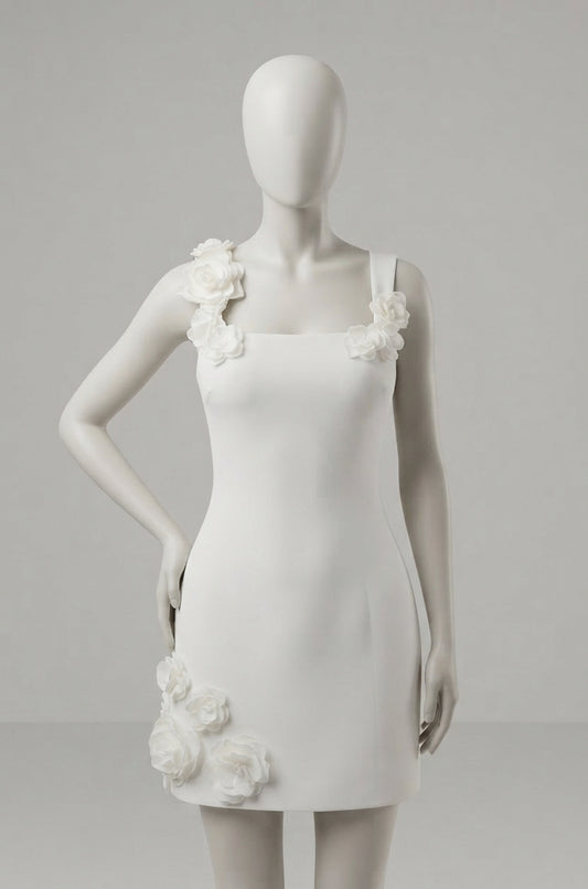 A white sleeveless mini dress with 3D floral rose embellishments on the shoulders and lower skirt, displayed on a white mannequin against a light gray background.