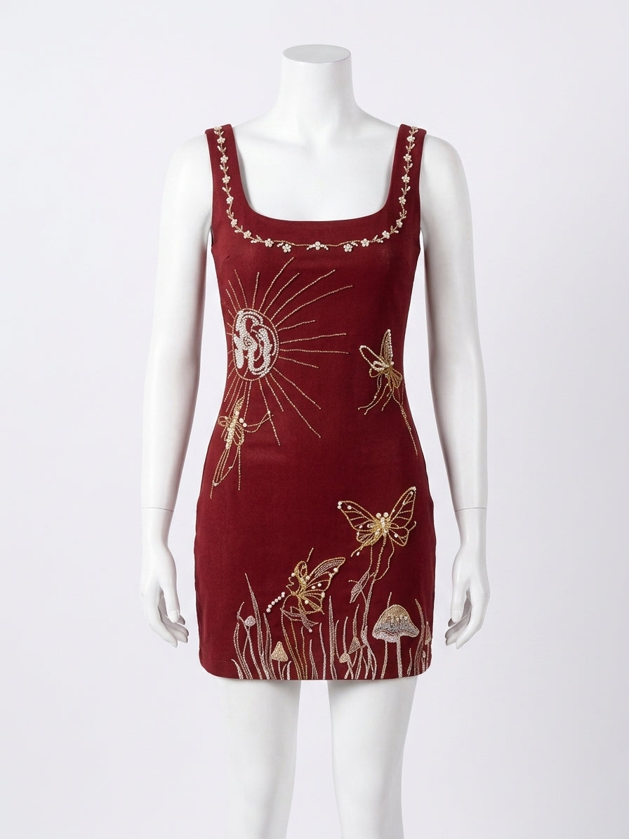 A sleeveless burgundy velvet dress with gold embroidered butterflies, sun rays, and floral motifs, displayed on a white mannequin against a light gray background.