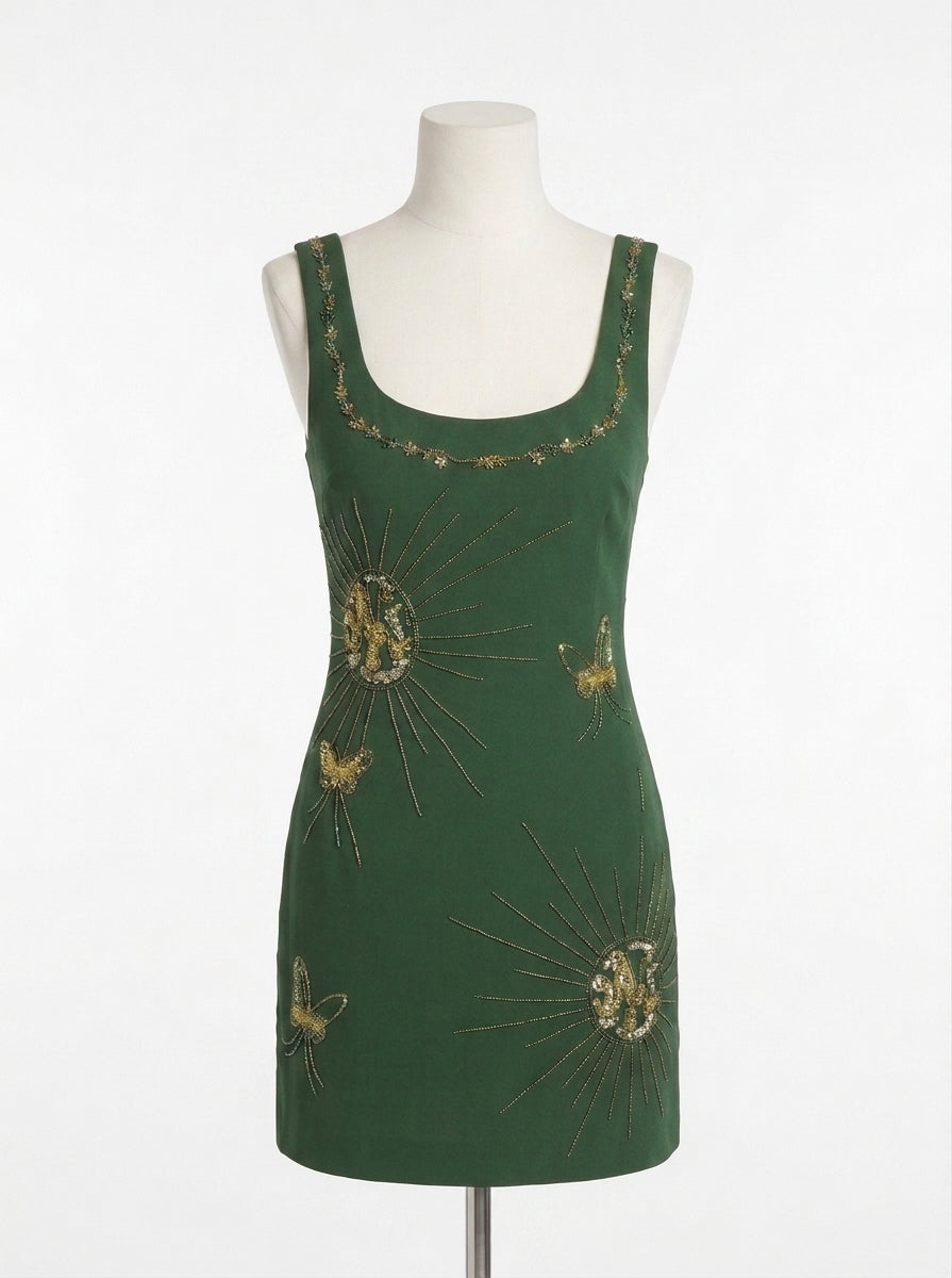 A dark green sleeveless dress displayed on a white mannequin torso against a plain white background. The dress features gold embroidered sunburst and butterfly motifs with a delicate gold floral border along the scoop neckline.