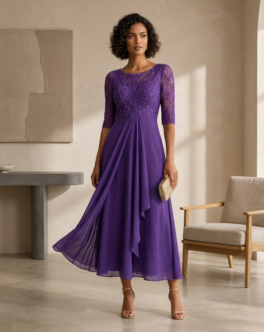 A woman models a purple lace and chiffon midi dress in a modern, sunlit room with a chair and console table.