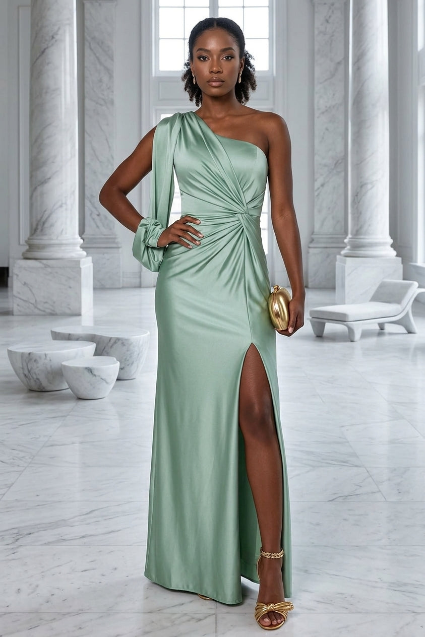 A woman models a floor-length sage green one-shoulder gown with a high thigh slit, styled with a small gold clutch and gold sandals in a grand marble-floored hall with columns.
