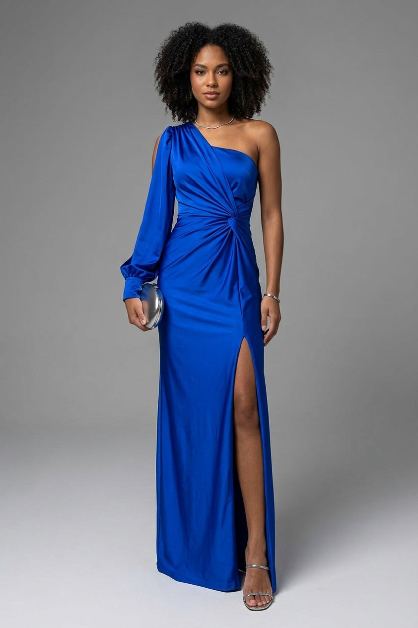 A woman modeling a royal blue one-shoulder satin maxi dress with a high thigh slit, standing against a neutral gray studio background.