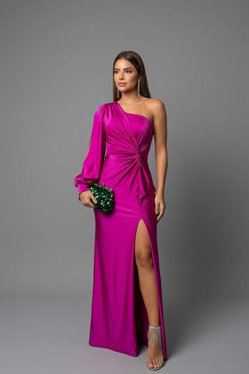 A woman models a vibrant magenta one-shoulder evening gown with a high thigh slit, holding a green beaded clutch against a solid gray studio background.