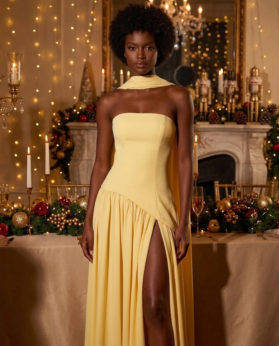 A woman modeling a pale yellow strapless gown with a high thigh slit, posed in front of a decorated Christmas table and fireplace background.
