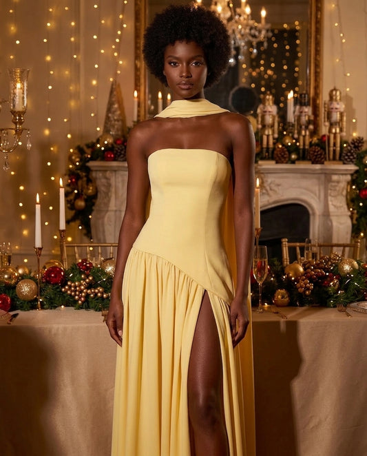 A woman modeling a pale yellow strapless gown with a high thigh slit, posed in front of a decorated Christmas table and fireplace background.