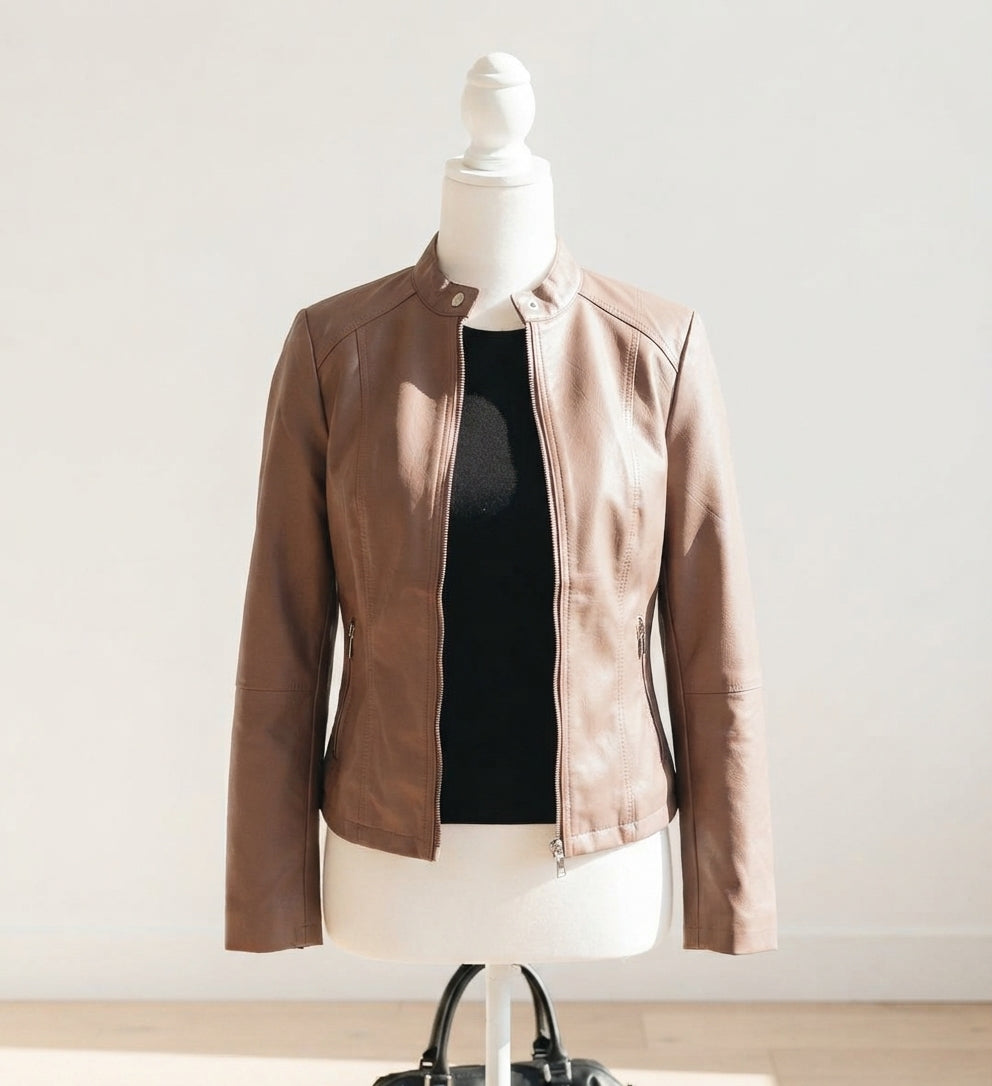 A light brown faux-leather moto jacket displayed on a white mannequin torso, layered over a black top, set against a plain off-white wall.