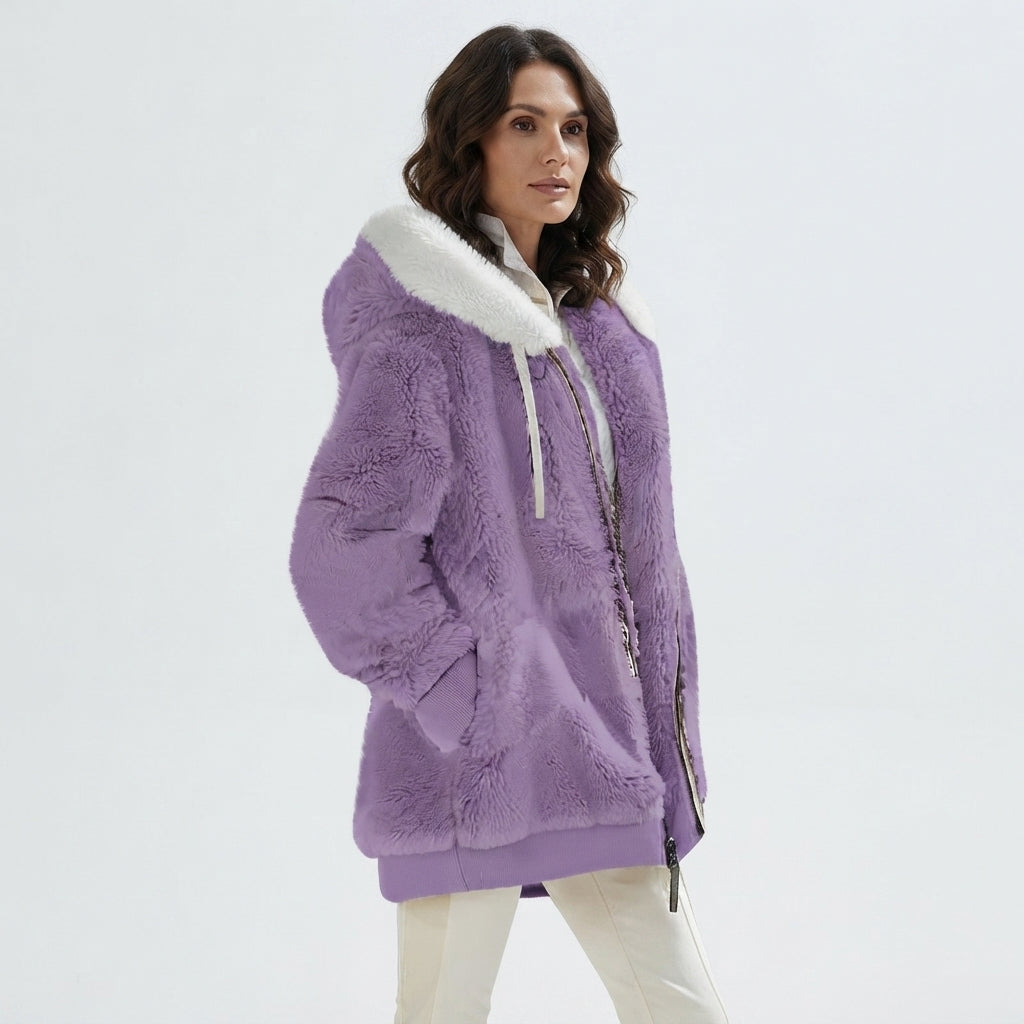 A woman wearing a lavender purple sherpa fleece hooded jacket with a white faux-fur collar and white drawstrings, paired with off-white pants, against a plain light gray studio background.