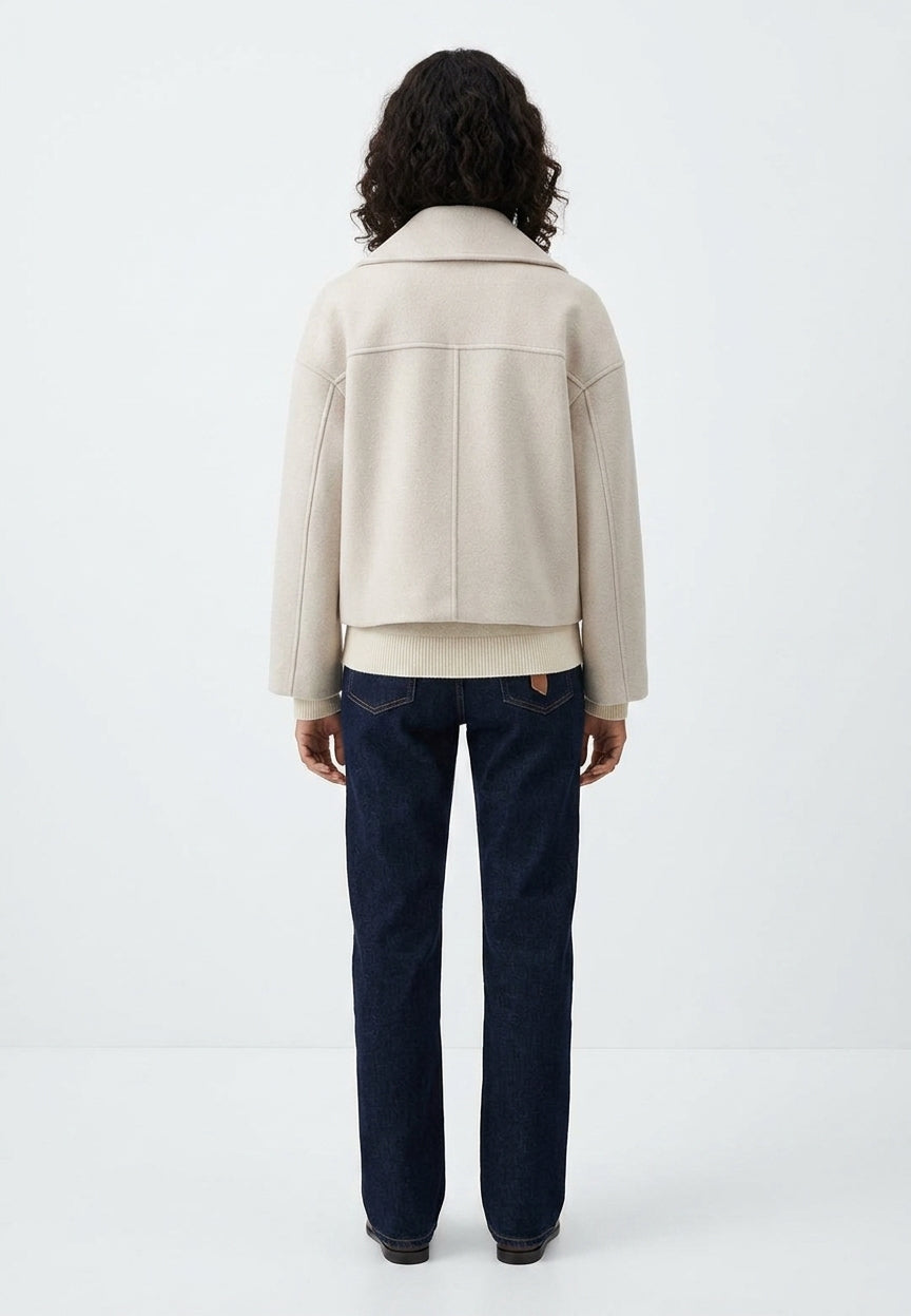 A model viewed from the back wearing a cropped beige jacket and dark blue jeans against a plain white studio background.
