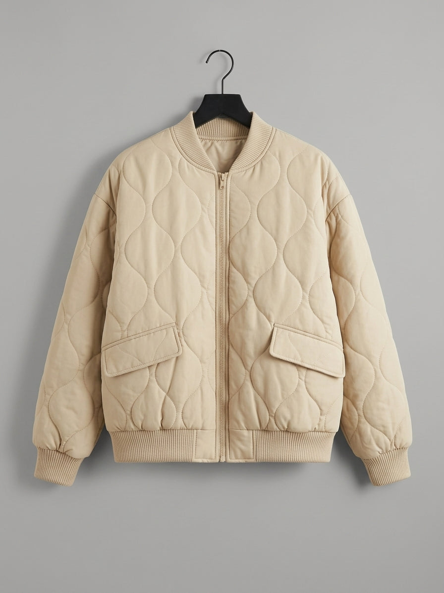 A quilted bomber jacket in a light cream or beige color, hanging on a black hanger against a solid gray background.