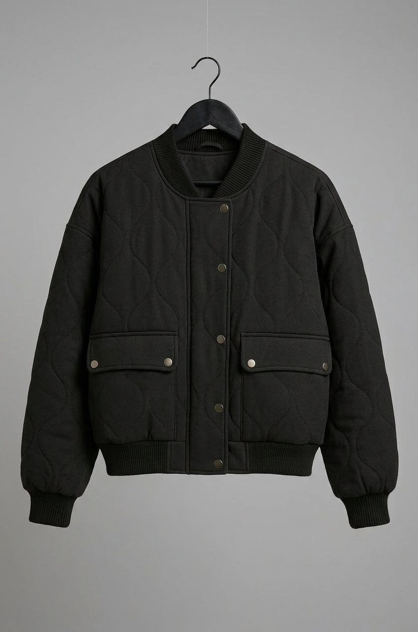 A black quilted bomber jacket with snap-button flap pockets, hanging on a black hanger against a solid gray background.
