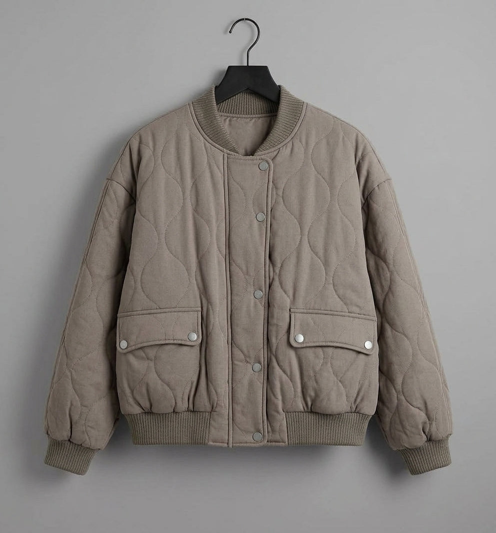 A taupe quilted bomber jacket hanging on a black hanger against a solid gray background.