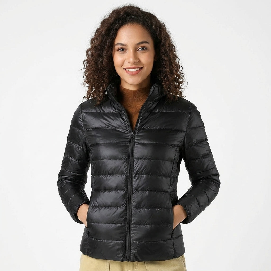 A woman with curly brown hair wearing a black puffer jacket, standing against a plain white studio background.