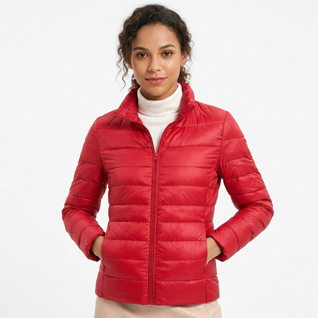 A woman wearing a bright red puffer jacket over a white turtleneck sweater, standing against a plain white studio background.