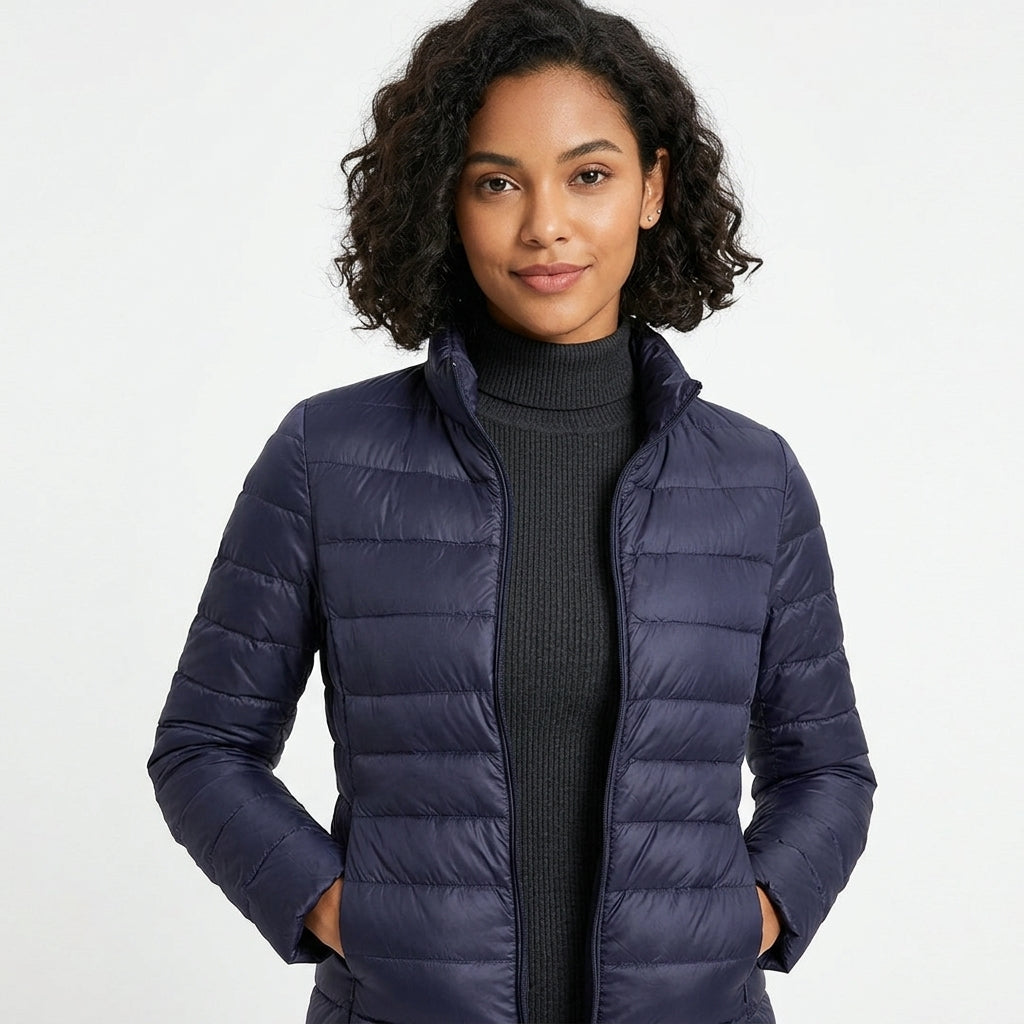A woman wearing a navy blue puffer jacket over a black ribbed turtleneck sweater, photographed against a clean white studio background.